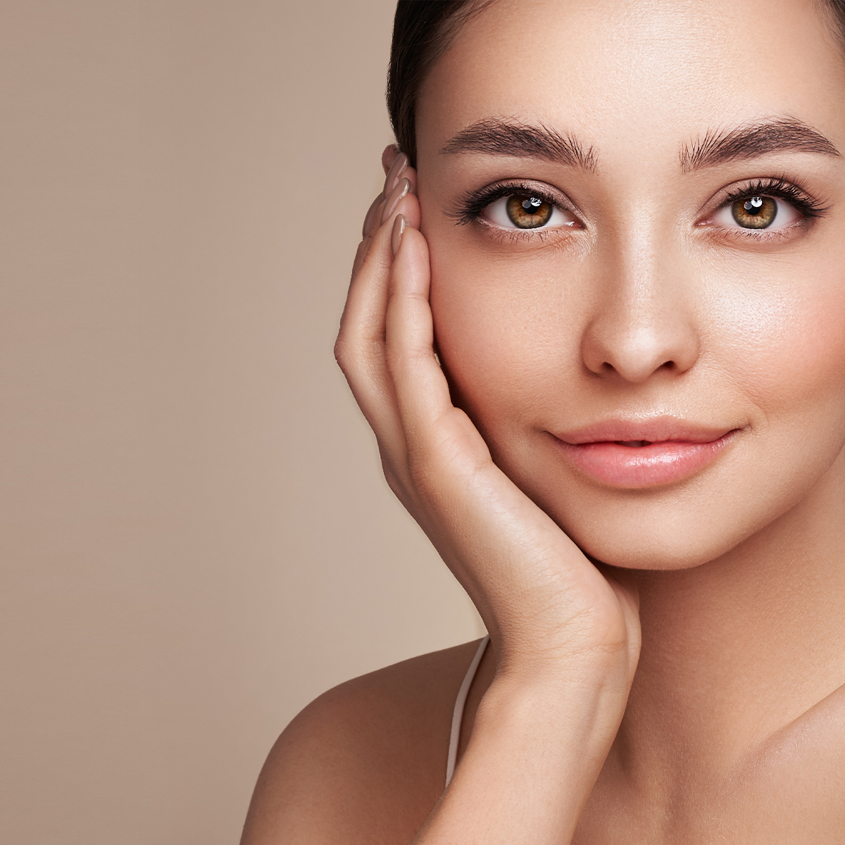 Tan woman with beautiful skin holding face and smiling into camera